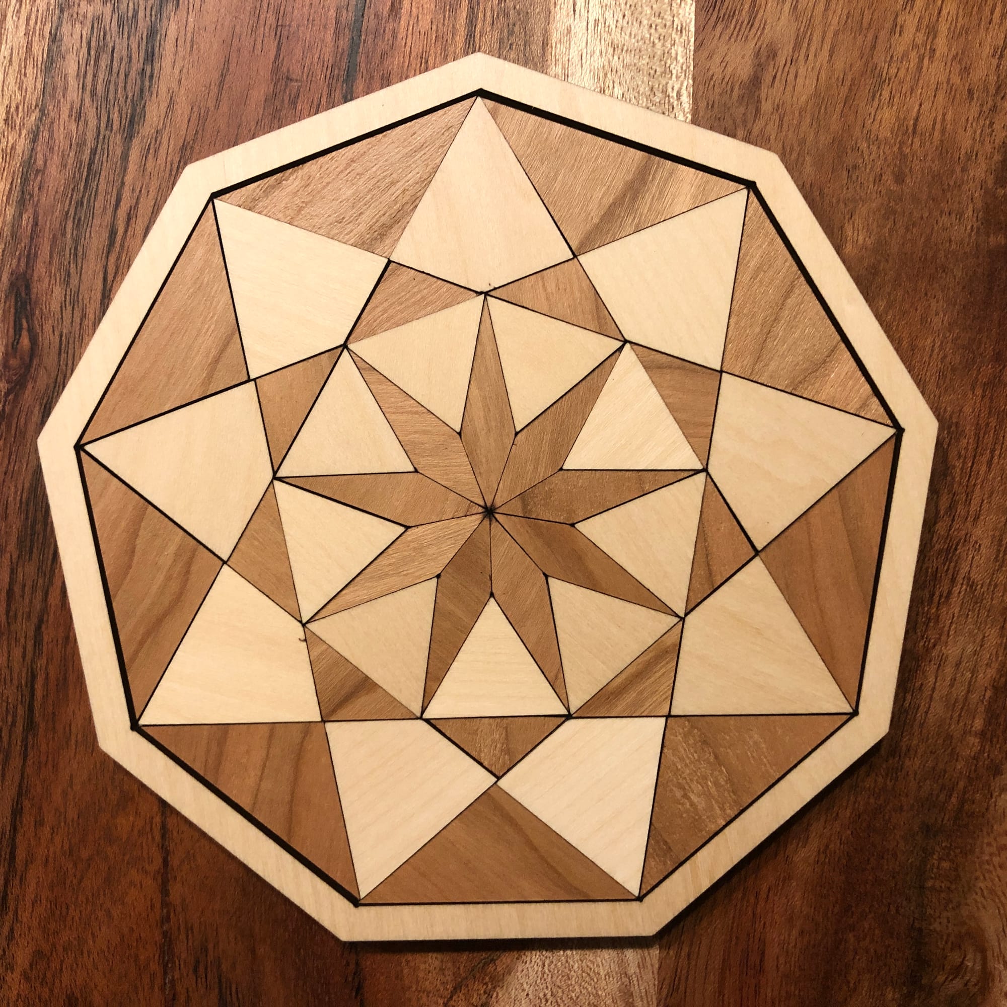 a wooden inlay of a nonagon with a star  in the center with kites and triangles alternating colors of wood