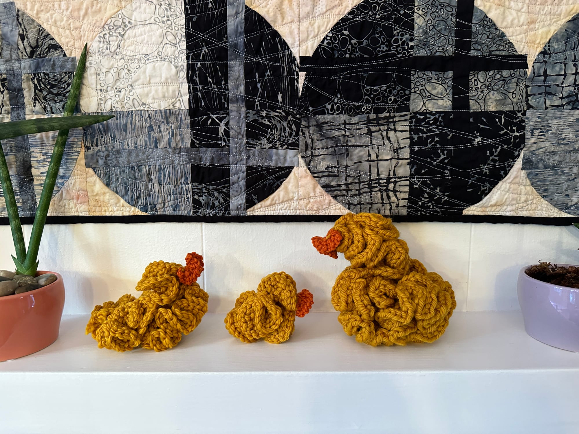 three crocheted hyperbolic ducks on a mantle with quilt and plans by them